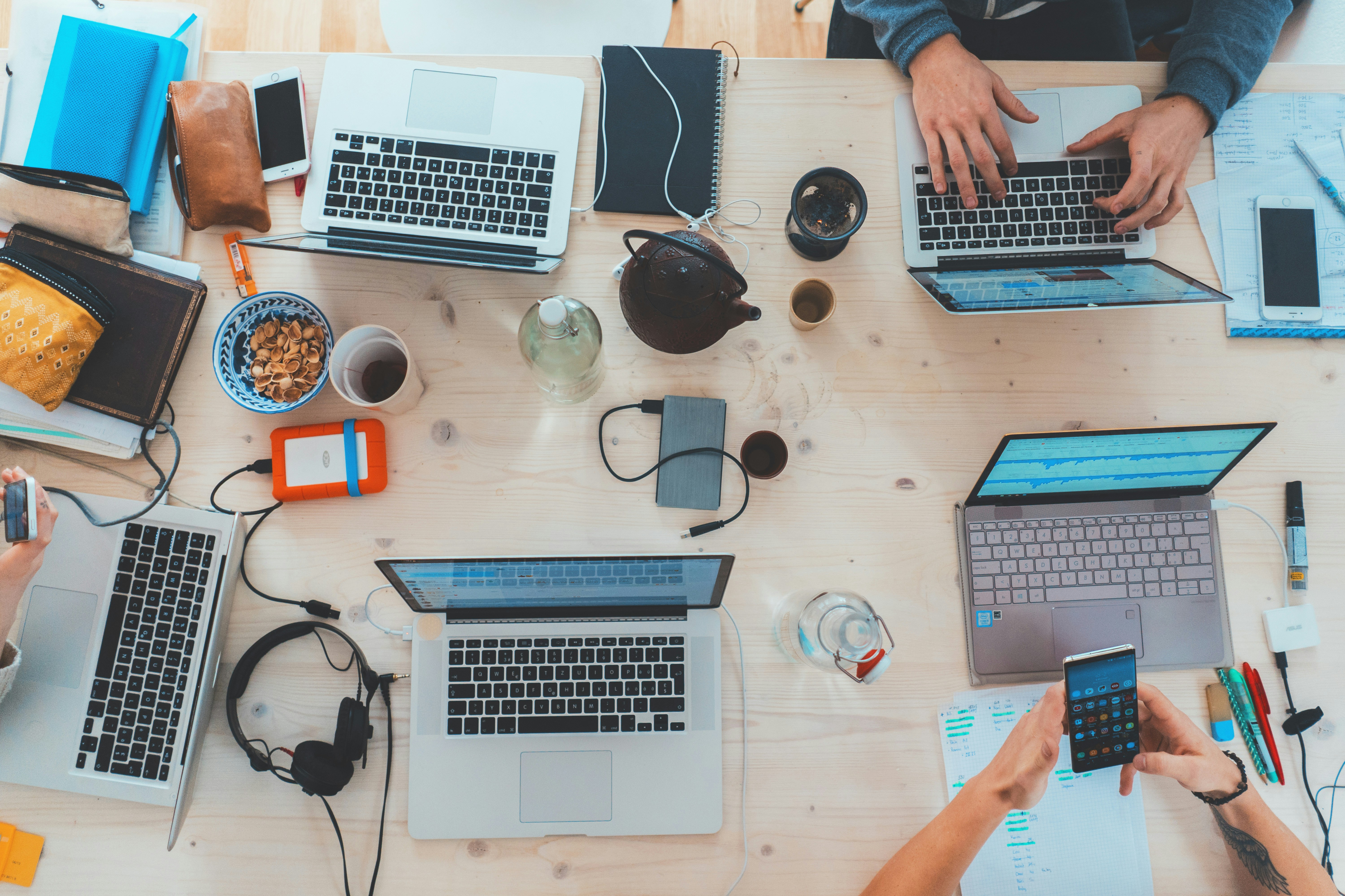 Escritório, rotina. Mesa com trabalhadores utilizando notebooks e cadernos